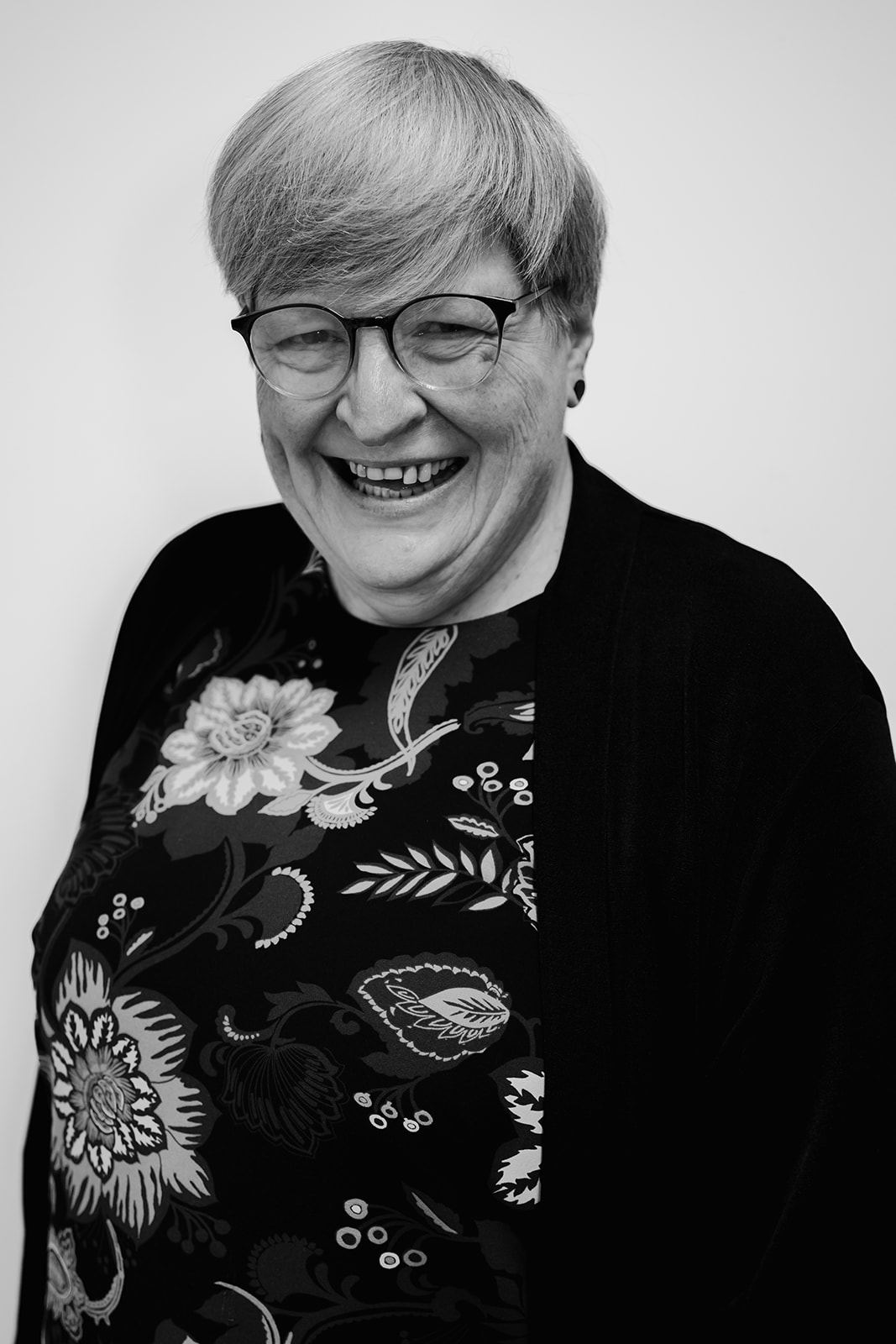 Smiling person with short hair and floral shirt.