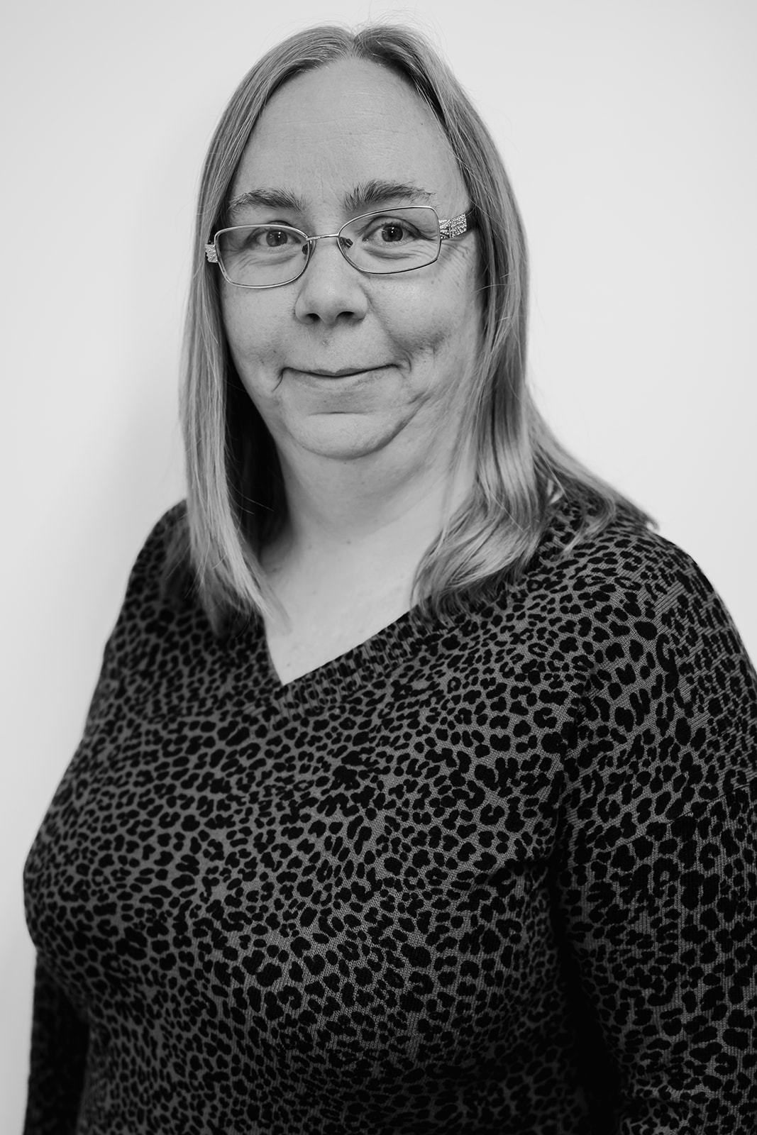 Woman wearing glasses and leopard print top, smiling.