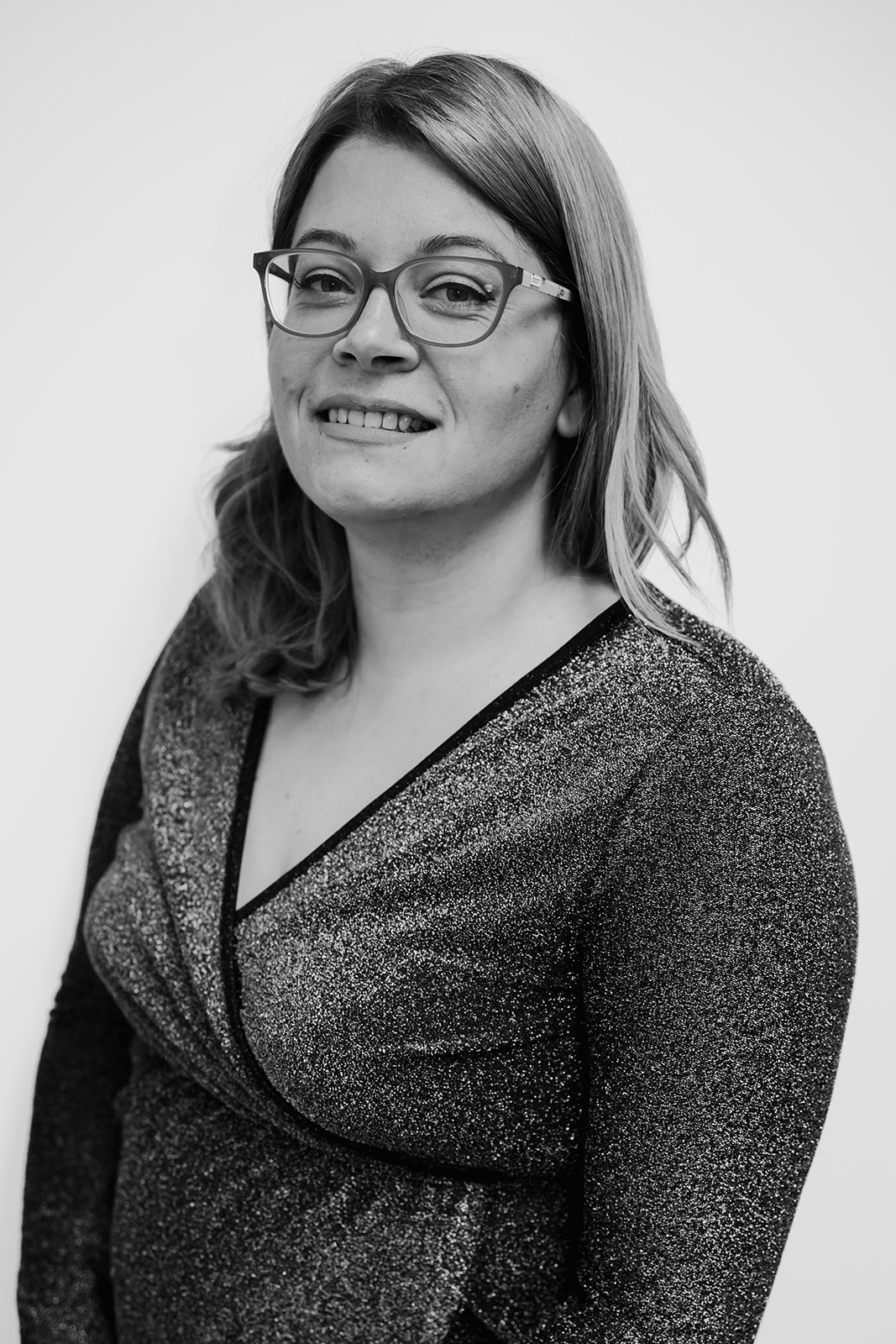 Smiling person in glasses and glittery top.